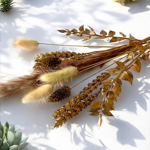May include: A bouquet of dried grasses and flowers in shades of brown and gold. The bouquet includes pampas grass, wheat, and dried leaves.