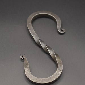 May include: Hand-forged, dark gray metal S-hook. The hook features a twisted central section and curled ends. This decorative hook is suitable for hanging items and adds a rustic touch to any space.