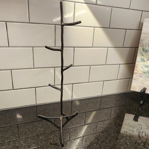 A black metal twig-shaped stand with five branches. The stand is on a black countertop with white subway tile behind it. A sign with the words 'Bless this home' is on the counter to the right of the stand.