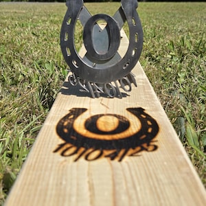 May include: A wooden horseshoe game set with a metal horseshoe target and a wooden board. The board has a horseshoe design and the numbers 10104125. The metal target has the letter "O" in the center.