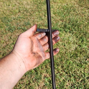 May include: A black metal fire poker with a twisted handle and a hook at the end. The poker is held in a hand with dirt on it.