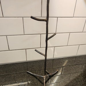 A black metal mug rack shaped like a tree with five branches. The rack is standing on a black countertop.
