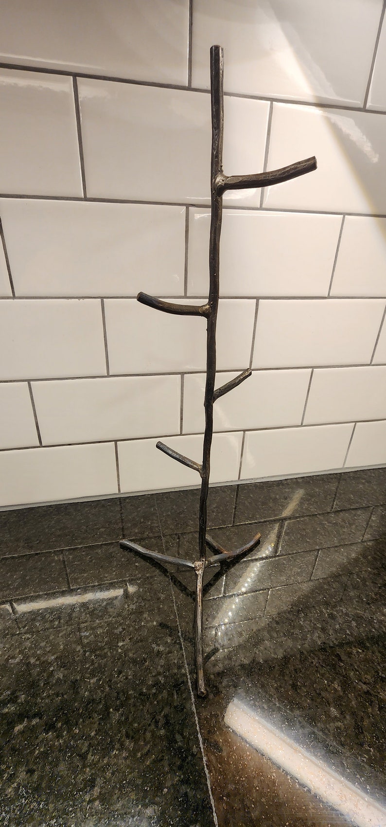 A black metal mug rack shaped like a tree with five branches. The rack is standing on a black countertop.