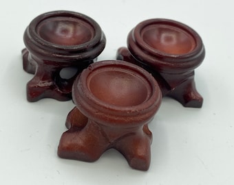May include: Three small, wooden display stands with a rounded top and three legs. The stands are a dark brown color.