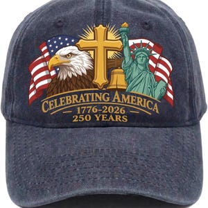 以下が含まれることがあります： 愛国的なデザインのネイビーブルーの野球帽。帽子には、アメリカ国旗、金の十字架、鐘、自由の女神が描かれています。「Celebrating America 1776-2026 250 Years」の文字が前面にプリントされています。