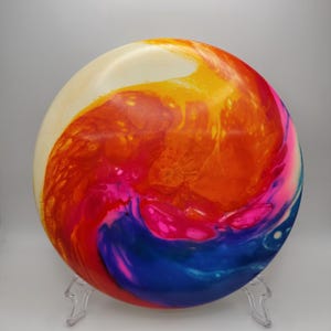 May include: A disc with a swirling pattern of yellow, orange, red, pink, and blue paint.