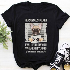 May include: Black t-shirt with a white graphic of a French bulldog holding a sign that says "I will follow you wherever you go, bathroom included".