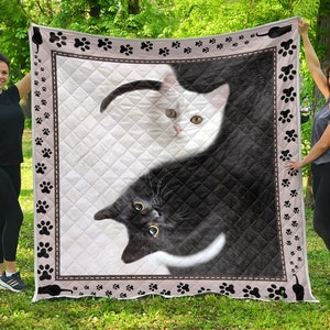 May include: A white and black cat quilt with paw prints around the border. The cats are in a yin yang design, with the white cat on the left and the black cat on the right.