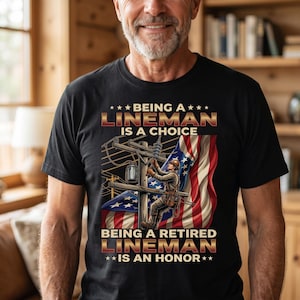 May include: Black t-shirt with a graphic of a lineman working on a power pole, set against an American flag. The text reads "Being a Lineman is a Choice, Being a Retired Lineman is an Honor."