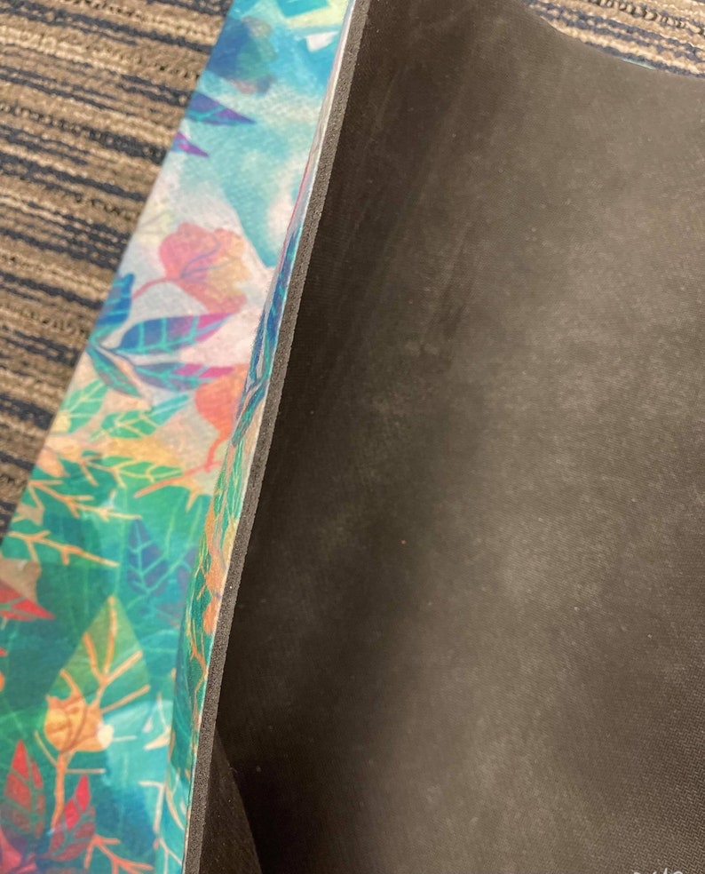 May include: A yoga mat with a colorful floral pattern on one side and a black non-slip surface on the other side.
