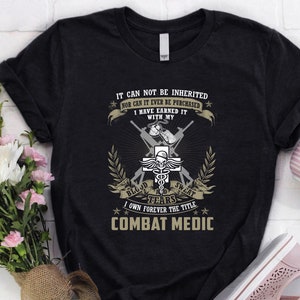 Puede incluir: Una camiseta negra con un diseño gráfico de un símbolo de caduceo médico con rifles cruzados y el texto "IT CAN NOT BE INHERITED NOR CAN IT EVER BE PURCHASED I HAVE EARNED IT WITH MY BLOOD TEARS SWEAT I OWN FOREVER THE TITLE COMBAT MEDIC".