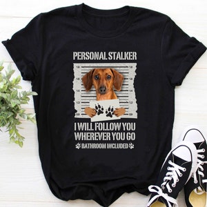 K&ouml;nnte beinhalten: Schwarzes T-Shirt mit einem Dackel, der ein Fahndungsfoto tr&auml;gt. Der Text lautet "PERSONAL STALKER" und "I WILL FOLLOW YOU WHEREVER YOU GO BATHROOM INCLUDED".