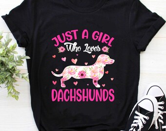May include: Black t-shirt with pink text that reads "Just a girl who loves dachshunds". The text is surrounded by pink hearts and a floral dachshund.