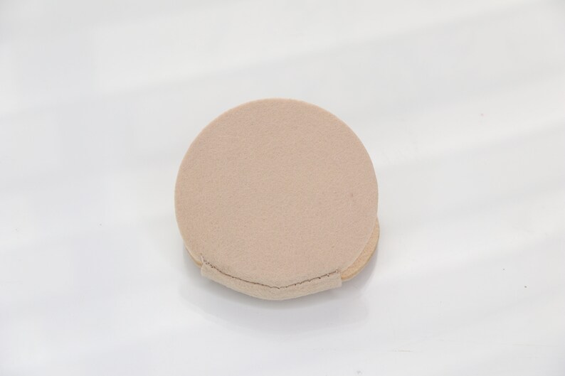 May include: A round, beige makeup sponge with a slightly textured surface.