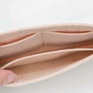 May include: Beige felt bag organizer with multiple compartments. The organizer has a soft, plush texture and is designed to fit inside a larger bag.