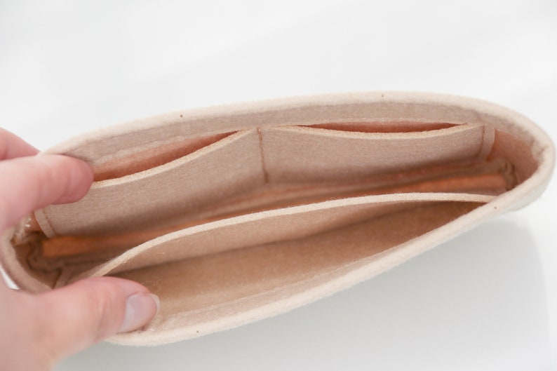 May include: Beige felt bag organizer with multiple compartments. The organizer has a soft, plush texture and is designed to fit inside a larger bag.