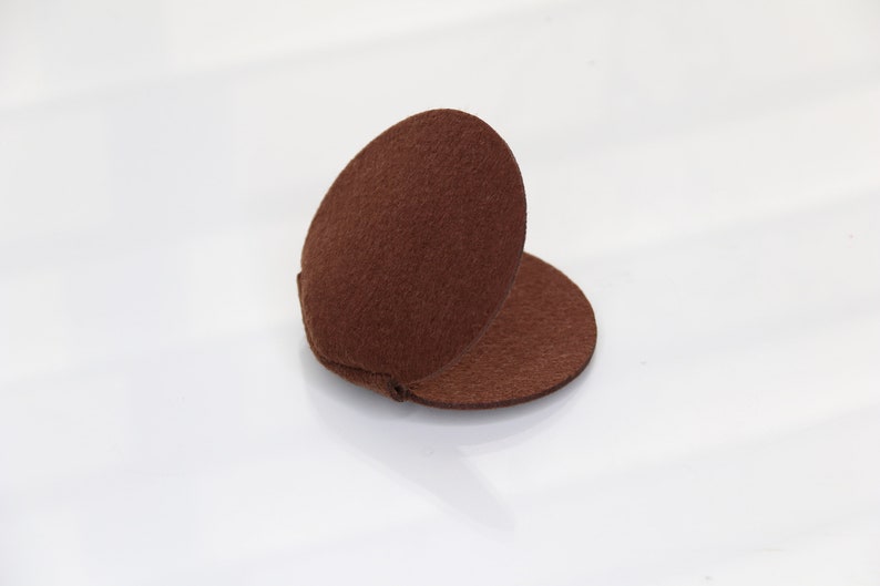 May include: A brown felt circle folded in half, creating a rounded shape. The felt is soft and textured.