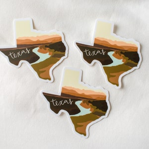 Puede incluir: Tres pegatinas con la forma de Texas, cada una con un dise&ntilde;o de paisaje. El dise&ntilde;o incluye un r&iacute;o, monta&ntilde;as y la palabra "texas" en una fuente de escritura. La paleta de colores incluye tonos de marr&oacute;n, verde y beige.