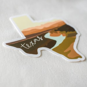 Puede incluir: Una pegatina con la forma de Texas, con un dise&ntilde;o de paisaje en tonos marrones, naranjas y verdes. La palabra "Texas" est&aacute; escrita en blanco en la imagen.