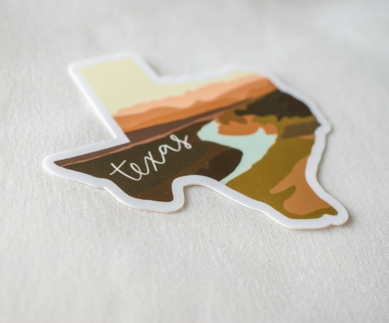 Puede incluir: Una pegatina con la forma de Texas, con un dise&ntilde;o de paisaje en tonos marrones, naranjas y verdes. La palabra "Texas" est&aacute; escrita en blanco en la imagen.