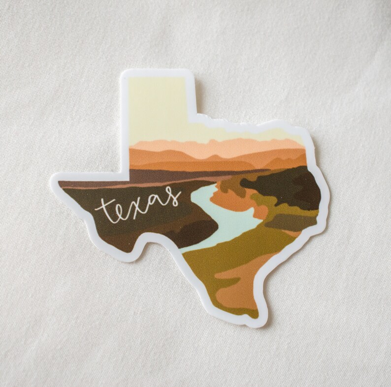 Puede incluir: Una pegatina con la forma de Texas, con un dise&ntilde;o de paisaje en tonos marrones, verdes y un r&iacute;o azul claro. La palabra "texas" est&aacute; escrita en cursiva.