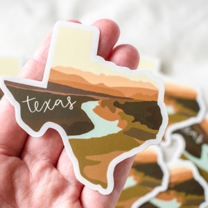 Puede incluir: Una pegatina con la forma del estado de Texas, con un dise&ntilde;o de paisaje en tonos marrones, beige y verdes. La palabra "Texas" est&aacute; escrita en cursiva en la pegatina.