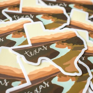 Puede incluir: Una colecci&oacute;n de pegatinas con forma de Texas. Cada pegatina presenta un dise&ntilde;o de paisaje en tonos marrones, beige y verdes, con la palabra "Texas" en una fuente manuscrita. Las pegatinas tienen un borde blanco.