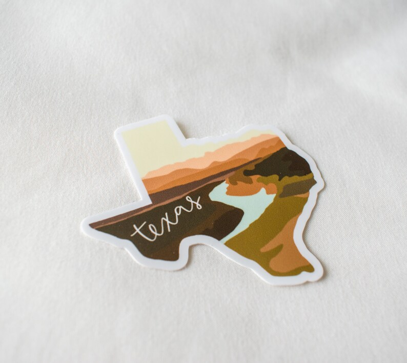 Puede incluir: Una pegatina con la forma de Texas, con un dise&ntilde;o de paisaje en tonos marrones, beige y azul claro. La palabra "texas" est&aacute; escrita en cursiva en la imagen.