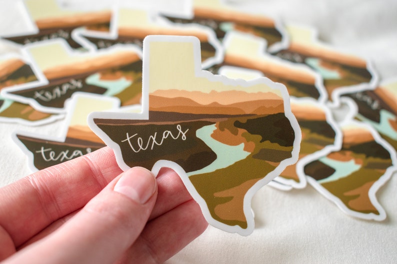 Puede incluir: Una colecci&oacute;n de pegatinas con forma de Texas. Cada pegatina presenta un dise&ntilde;o de paisaje con un r&iacute;o y monta&ntilde;as en tonos marrones, beige y verdes. La palabra "texas" est&aacute; escrita en cursiva en cada pegatina.