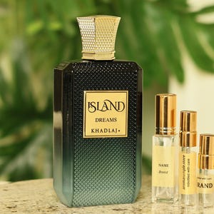 May include: A black and teal perfume bottle with a gold cap and the words "ISLAND DREAMS KHADLAJ" on the label. Several small sample bottles with gold caps and labels are next to the perfume bottle. The background is a green leafy plant.