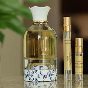 May include: A collection of perfume bottles and vials. A large perfume bottle with a white floral-shaped cap and a blue and white floral design on the base. Several smaller vials with gold caps are arranged next to it.