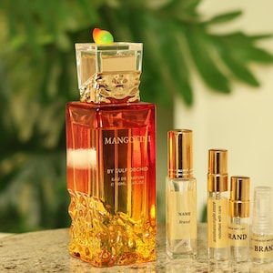 May include: A perfume bottle with a square, orange-to-yellow gradient design, topped with a decorative cap. Several smaller sample bottles and vials are arranged in front of the perfume bottle. The text "MANGO" is visible on the perfume bottle.