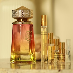 May include: A perfume bottle with a gold cap and a gradient peach and yellow body. Several small sample vials are arranged to the right. The bottle is labeled "KHADLA" and "PEACH CORNER".