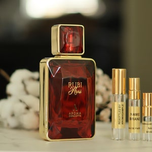 May include: A red glass bottle of perfume with a gold cap and label that reads "Rubi Airi" and "Aroma Concepts". Three smaller glass bottles of perfume are also shown, each with a gold cap and label.
