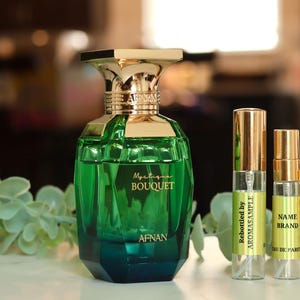May include: A green glass bottle of Mystogan Bouquet perfume by Afnan. The bottle has a gold cap and a gold label with the name of the perfume and the brand. There are also four smaller bottles of perfume in the image, all with gold caps and labels.