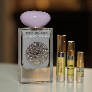 May include: A clear glass bottle of perfume with a light purple lid. The bottle is labeled 'MUSK COLLECTION MYSTERIOUS TAHARA BY GULF ORCHID'. Three smaller bottles of perfume are also visible, each with a gold cap and a label. The labels on the smaller bottles read 'Rebottled by AROMASAMPLE', 'NAME BRAND', and 'BOTTLER BY NAME BRAND'.