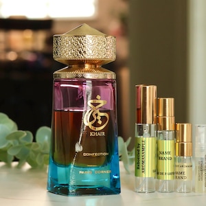 May include: A gold and blue glass bottle of perfume with a gold cap. The bottle is labeled "Khair Confection" and "Paco Corner". There are three smaller perfume bottles next to it, labeled "Aromasample", "Name Brand", and "Name Brand".
