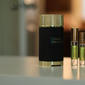 May include: A black and gold bottle of perfume with the text "CODE VERDE SUCRE" on the front. There are three smaller bottles of perfume next to it.