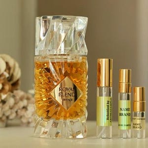 May include: A perfume bottle with a faceted crystal top and a gold label that reads "ROYAL BLEND VINTAGE." Three smaller sample bottles with gold caps and labels are next to the perfume bottle. The bottles are filled with a golden liquid.