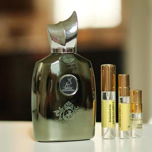 May include: A silver and green bottle of perfume with a silver cap and a gold label that says "Maison Alhambra" and "Mercury". There are three smaller bottles of perfume in the background, each with a gold label that says "Rebottled by Aromasample".