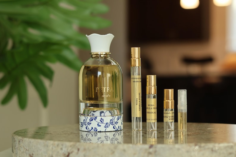 May include: A selection of perfume bottles and vials. A large perfume bottle with a white floral-shaped cap and a blue and white floral design on the base. Several smaller vials with gold caps are arranged beside it.