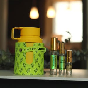 May include: A yellow reusable water bottle with a green leaf pattern and the text "ODYSSEY LIMONI" on the side. Four small glass bottles with gold caps and labels are in front of the water bottle.