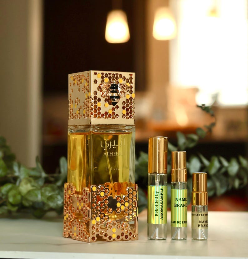 May include: A gold bottle of perfume with a bee design on the cap. The bottle is sitting on a gold honeycomb-shaped stand. There are three smaller bottles of perfume in the background, each with a different label.