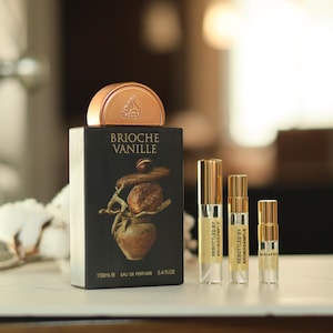 May include: A black bottle of Brioche Vanille Eau de Parfum with a gold cap and a gold label. The bottle is sitting on a table with three smaller bottles of perfume. The smaller bottles are labeled "Rebottled by AromaSample".