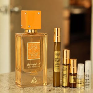 May include: A rectangular perfume bottle with an orange cap and gold accents, labeled "ANA ABIYEDH PASSION." Several smaller sample bottles are arranged to the right, with labels including "ROYAL MUSK" and "BERRY ON TOP."