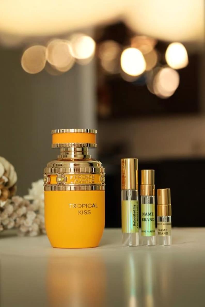 May include: A yellow bottle of perfume with a gold cap and the words "French Avenue" and "Tropical Kiss" on the label. There are three smaller bottles of perfume in the background.