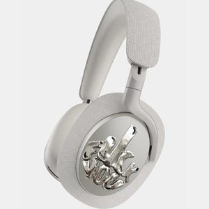Puede incluir: Auriculares blancos de diadema con un emblema plateado en la orejera. El emblema presenta un dise&ntilde;o abstracto. La diadema y las almohadillas est&aacute;n acolchadas con una tela texturizada. Los auriculares est&aacute;n sobre un fondo blanco.