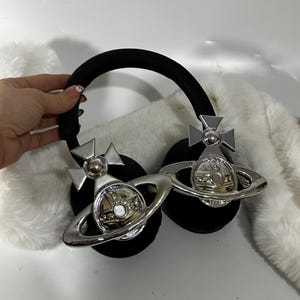May include: Black headphones with a silver orb and cross design on each earcup. The orb has a raised, circular centre and a ring around it.