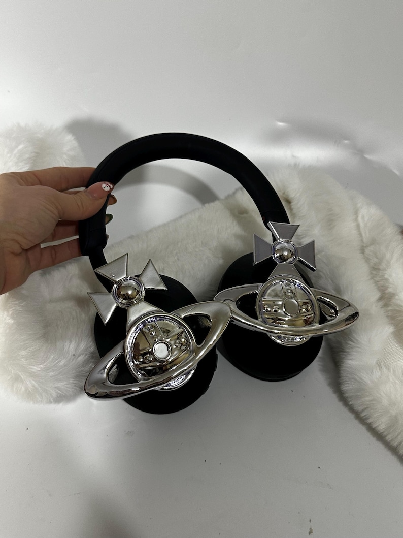 May include: Black headphones with a silver orb and cross design on each earcup. The orb has a raised, circular centre and a ring around it.