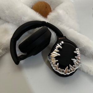 May include: Black wireless headphones with a silver, sharp, tooth-like design on one earcup. The headphones have the word "SONY" printed on the side.